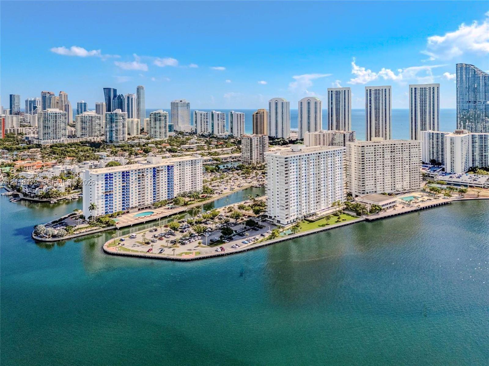 Waterfront aerial perspective featuring multiple high-rise structures, paved parking areas, and an expansive bay shoreline