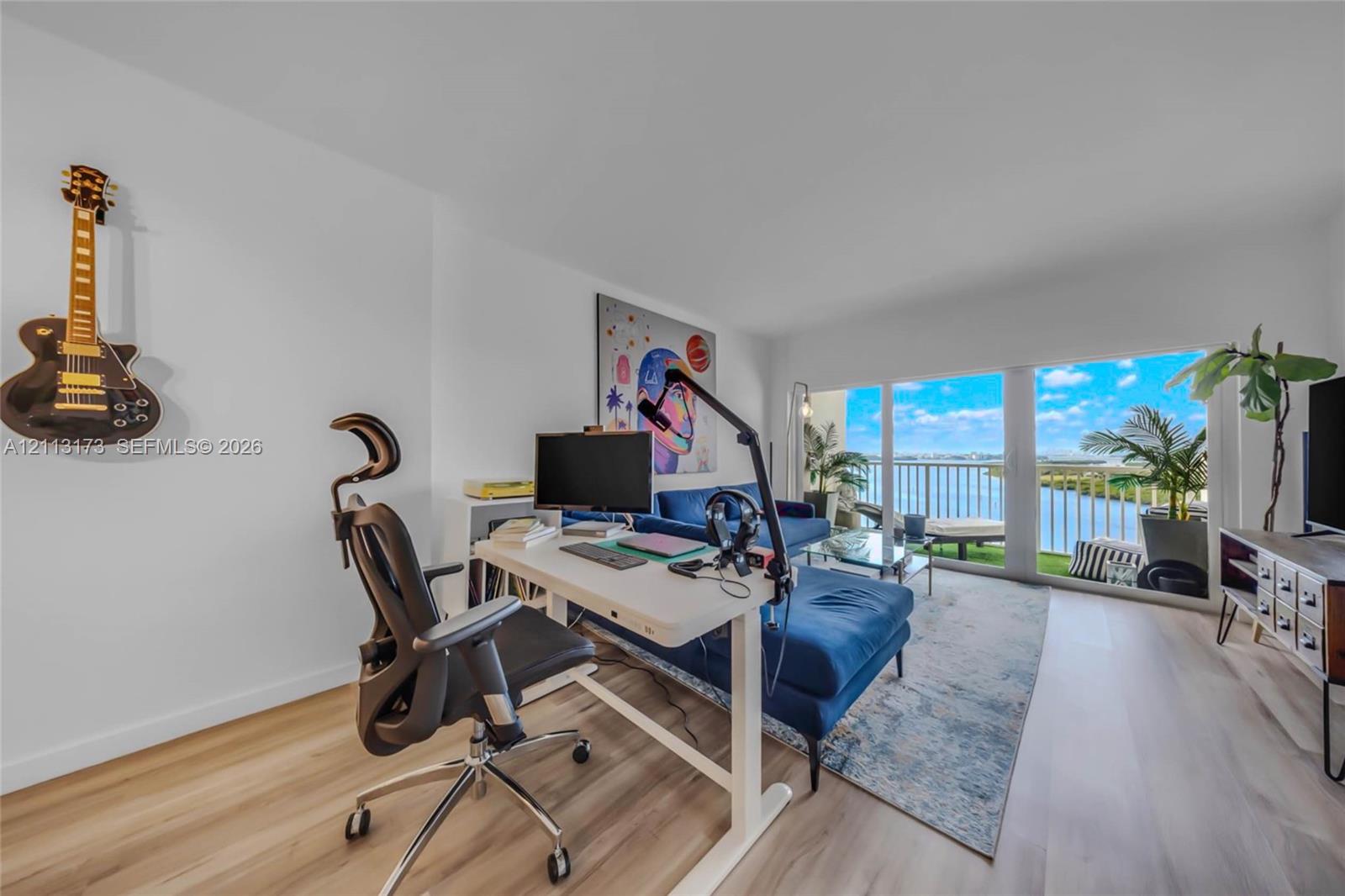 Light-filled living area featuring wood-finish flooring and floor-to-ceiling glass doors opening to a balcony with waterfront scenery