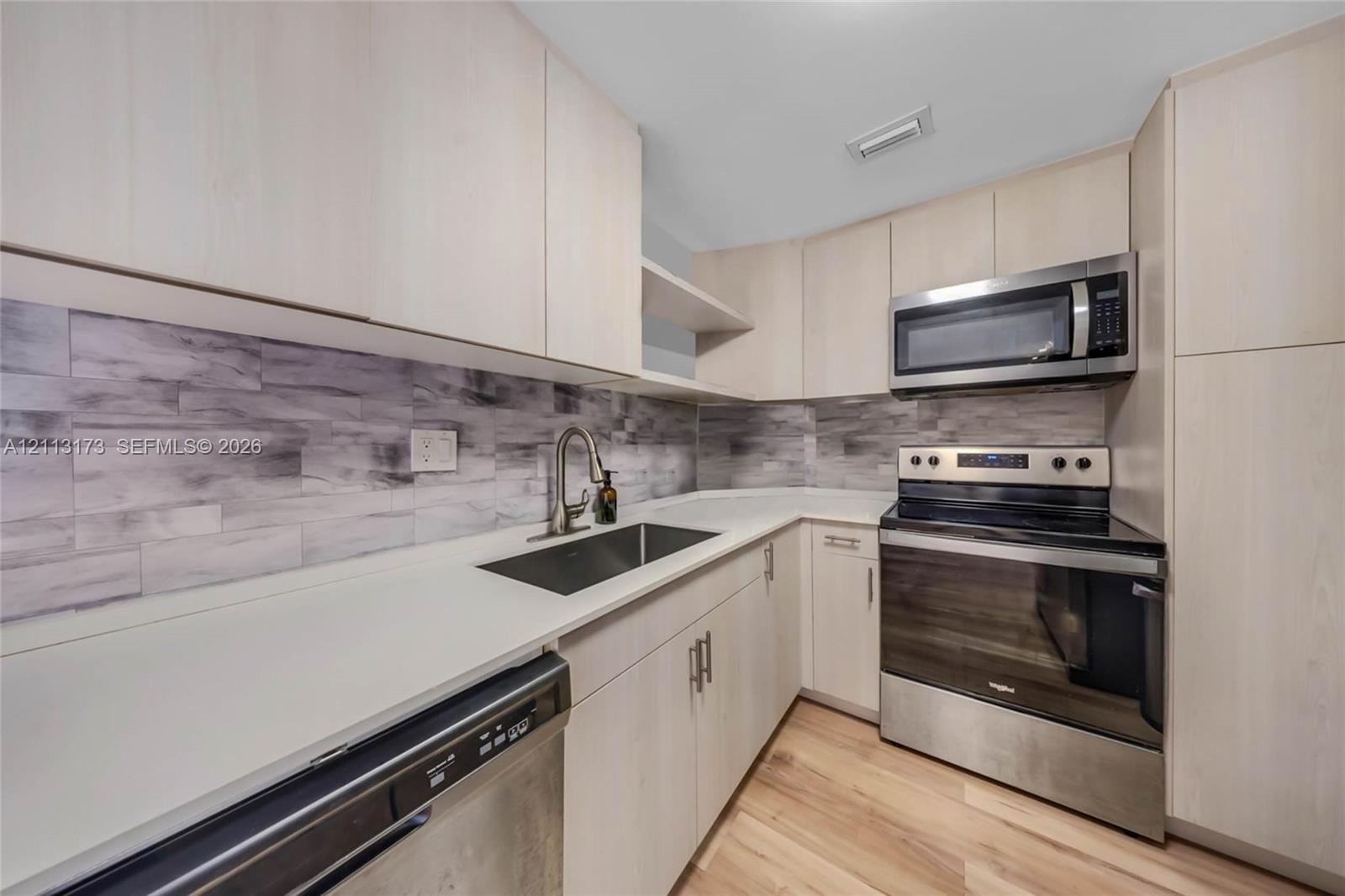 Kitchen featuring light-toned cabinetry, solid surface countertops, stainless steel appliances, and a horizontal tile backsplash