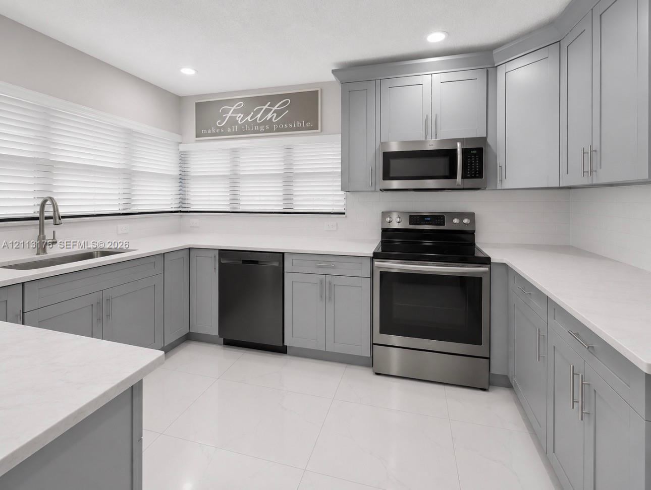 Kitchen featuring light gray shaker cabinetry, white solid-surface countertops, stainless steel appliances, and large-format tile flooring