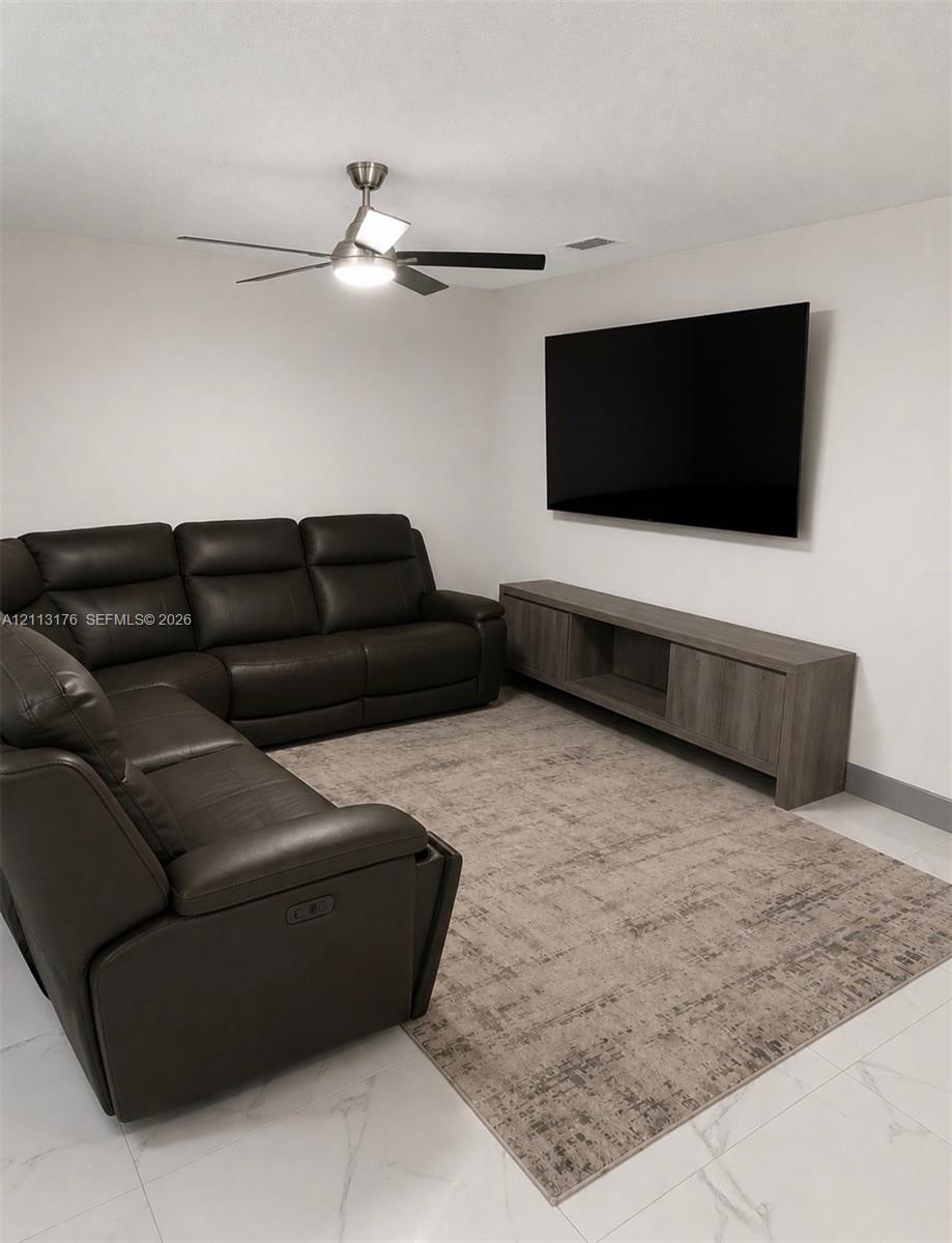 Neutral-toned room featuring large-format tile flooring and a brushed metal ceiling fan with integrated lighting