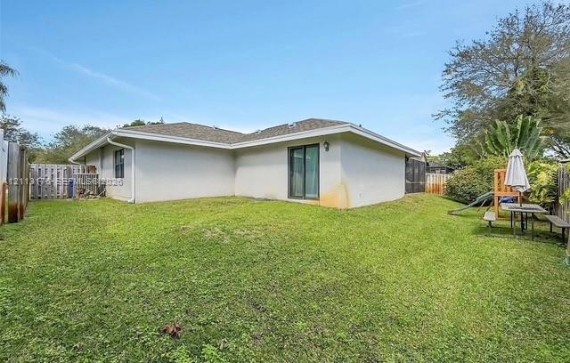 Stucco exterior featuring a hipped roof, glass sliding door, and enclosed backyard with wood-style fencing