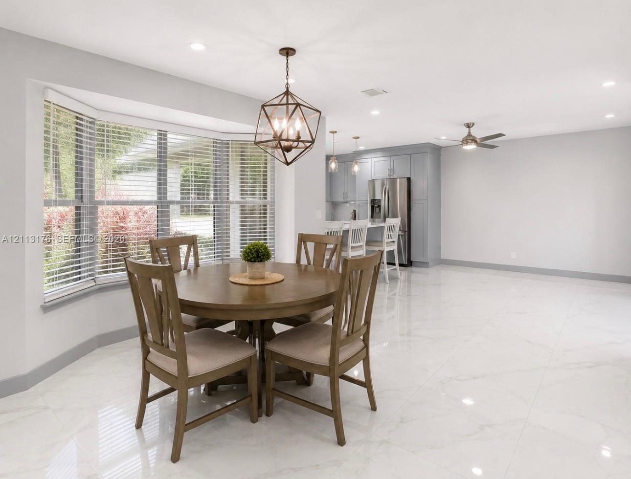 Open-concept space featuring polished stone-look tile flooring, bay window with slatted blinds, geometric pendant lighting, and recessed ceiling lights
