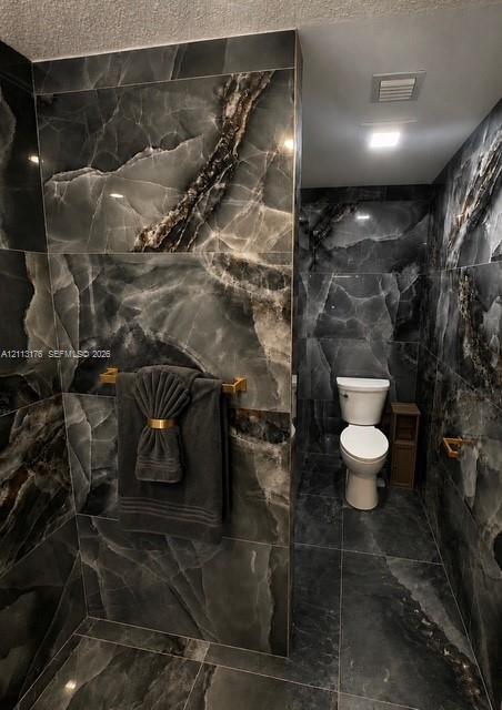 Full-height charcoal stone-finish wall tile with high-contrast veining, integrated recessed lighting, and brushed gold-tone hardware fixtures
