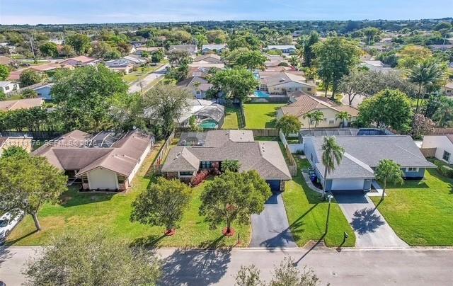 Aerial perspective of a single-story residence featuring a shingled roof, an attached garage, a paved driveway, and established landscaping including mature trees and lawn