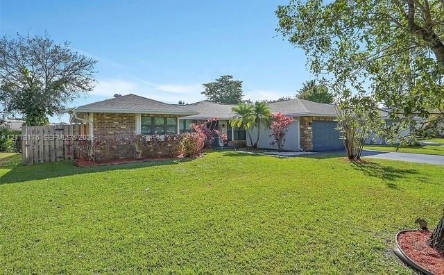 Single-story residence featuring a brick and stucco exterior, expansive lawn, mature landscaping, multi-car garage, and wood fencing