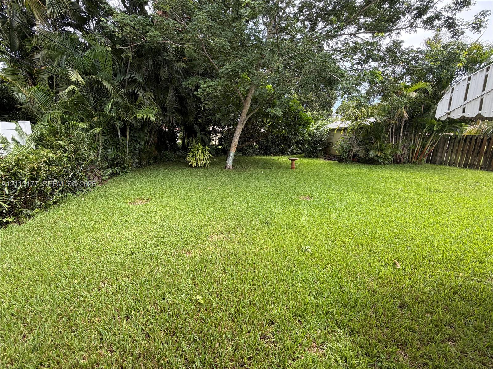 Private backyard featuring a manicured lawn, established landscaping, mature canopy trees, and perimeter wooden fencing