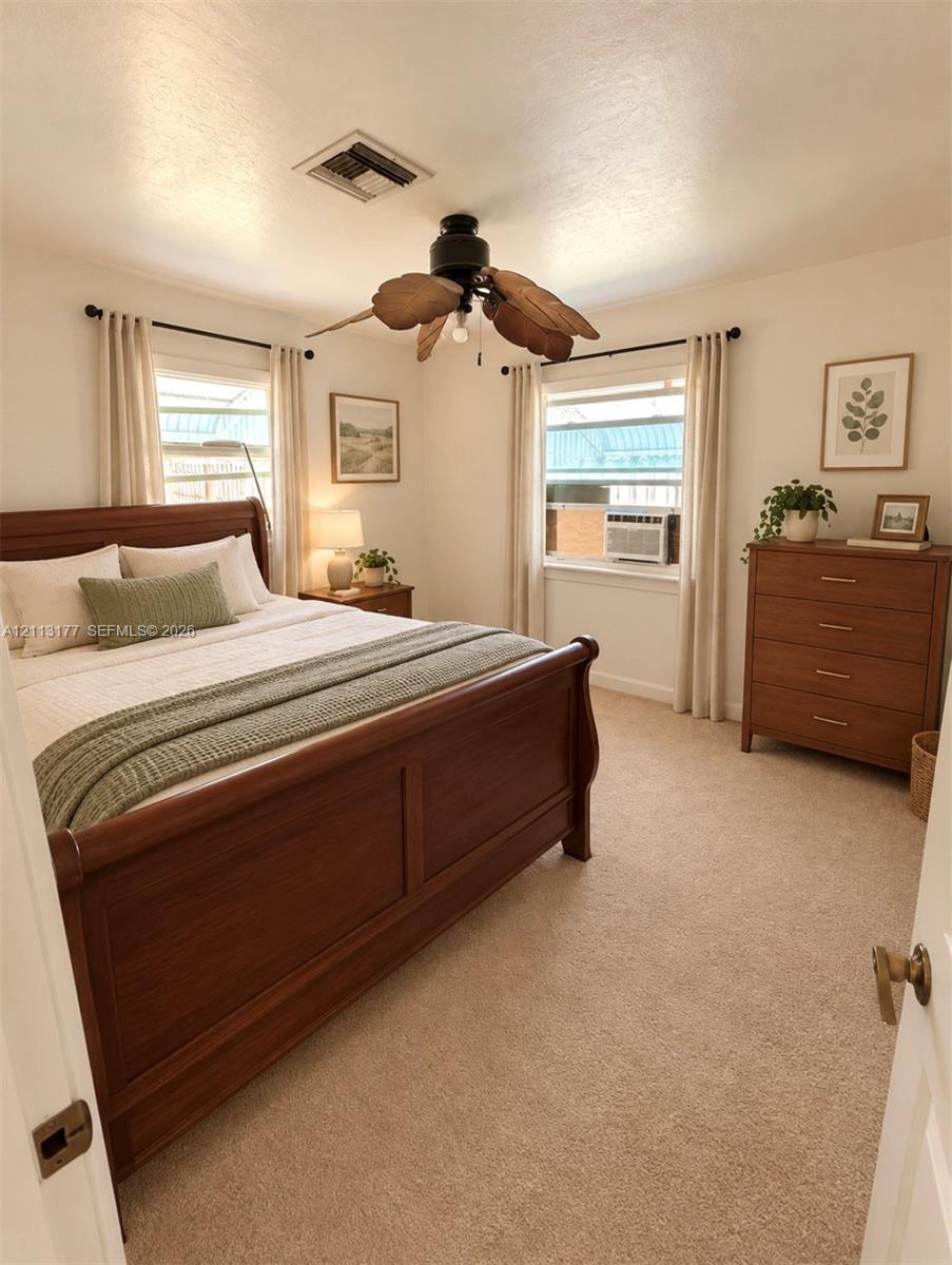 Neutral-toned carpeting, dual windows with curtain rods, and a ceiling fan with leaf-shaped blades