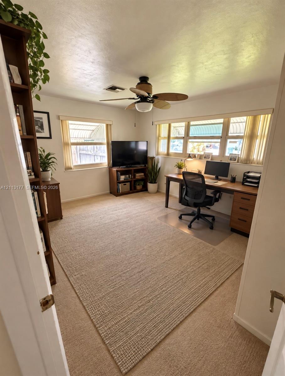 Room featuring neutral wall-to-wall carpeting, abundant natural light from multi-pane windows, and a ceiling-mounted light fixture with a five-blade fan