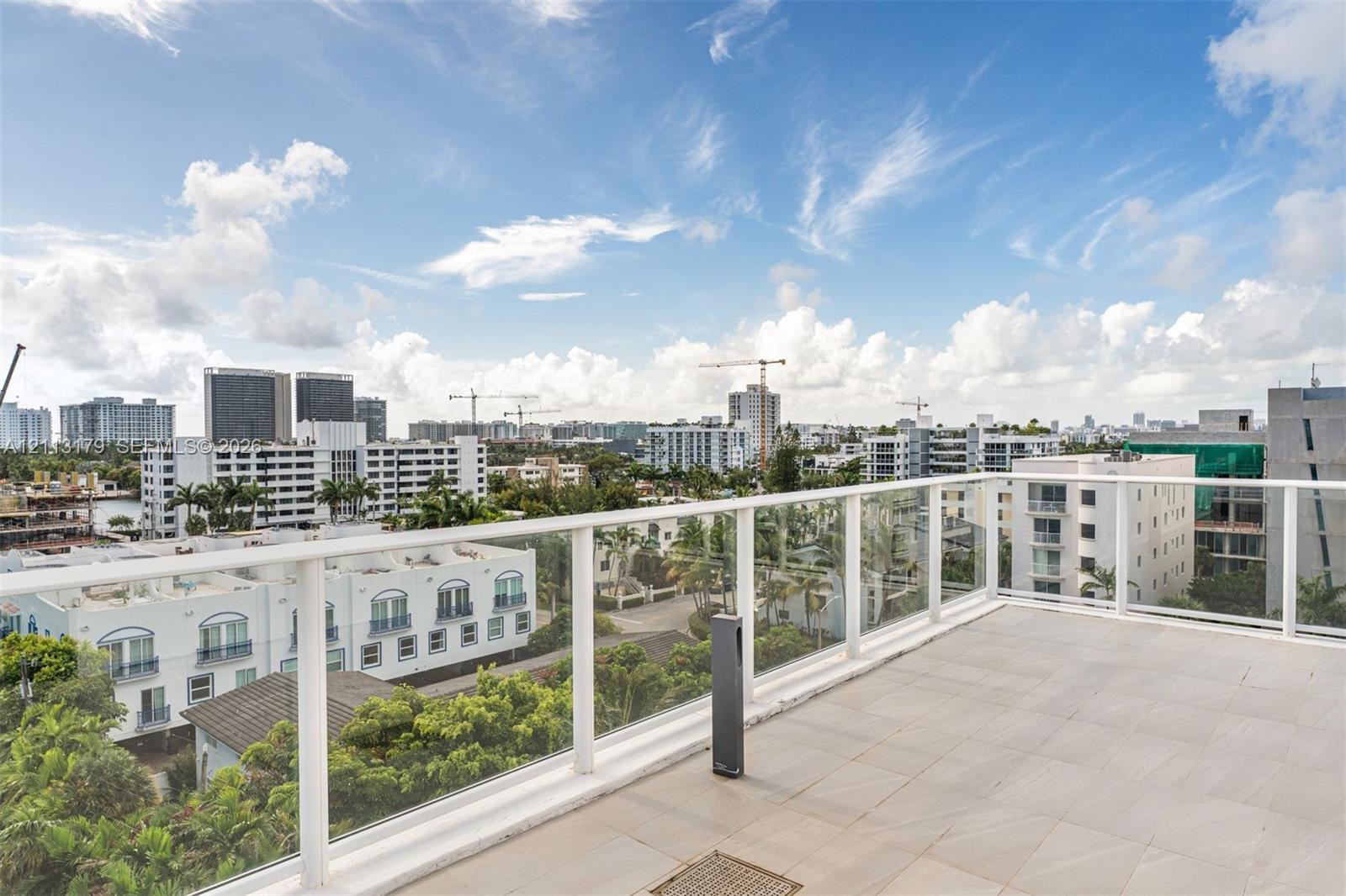 Expansive private balcony featuring oversized neutral floor tiling, a sleek glass-panel railing, and integrated lighting