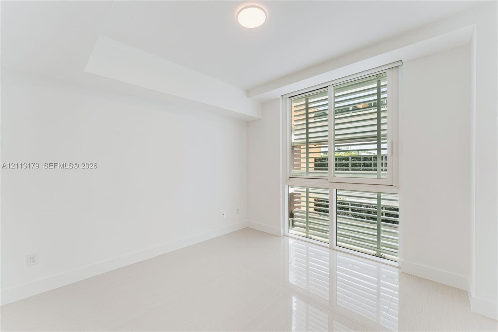 Room featuring polished tile flooring, white walls, recessed ceiling lighting, and large sliding windows with exterior horizontal louvers