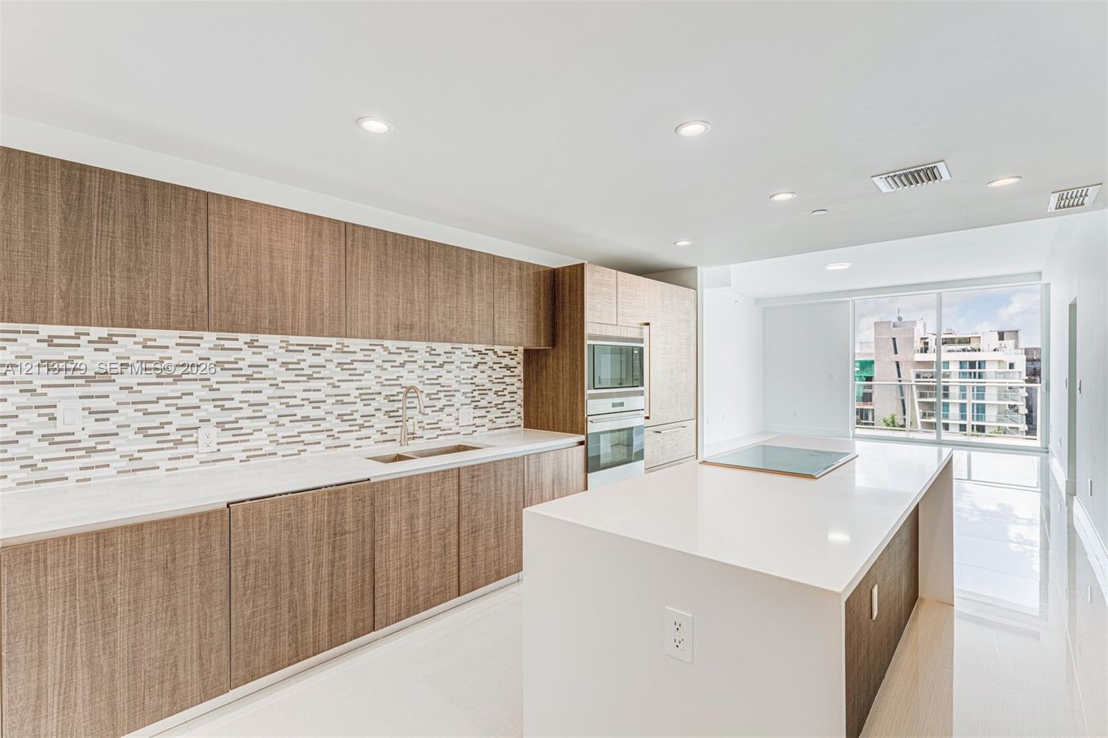 Kitchen featuring wood-finish cabinetry, quartz countertops, mosaic tile backsplash, built-in wall oven and microwave, and a large center island with an integrated cooktop Kitchen featuring wood-finish cabinetry, quartz countertops, mosaic tile backsplash, built-in wall oven and microwave, and a large center island with an integrated cooktop