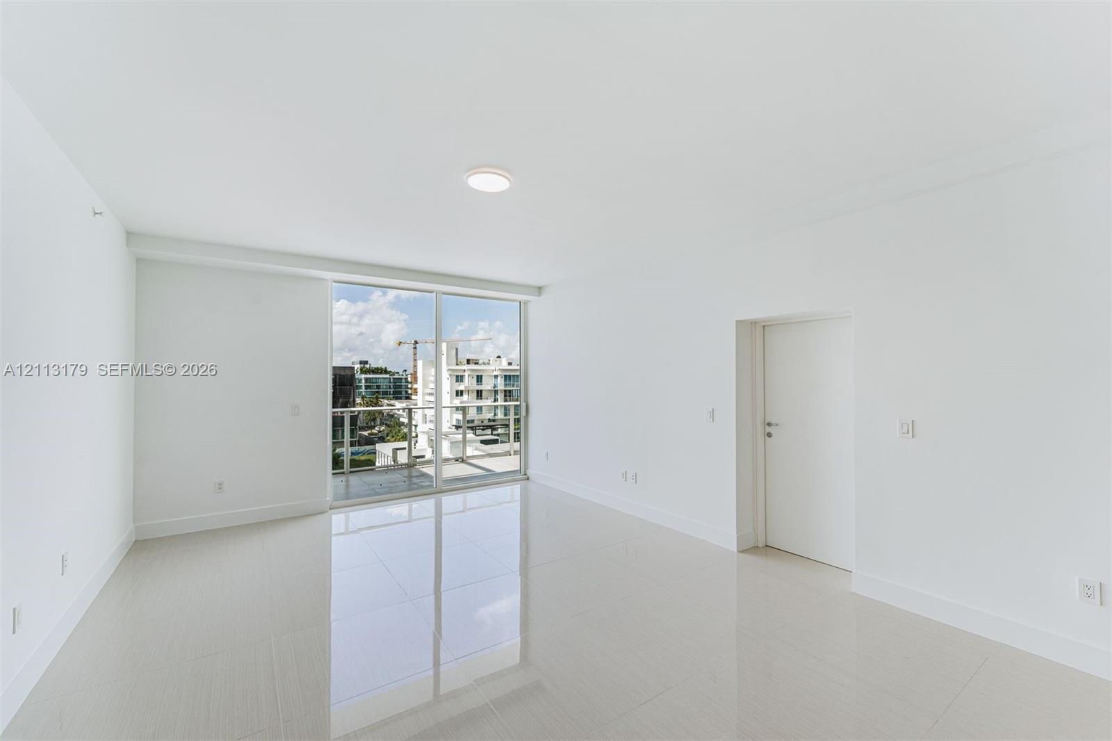 Open-concept room featuring light-toned tile flooring, recessed ceiling lighting, and sliding glass doors with access to a glass-railed balcony