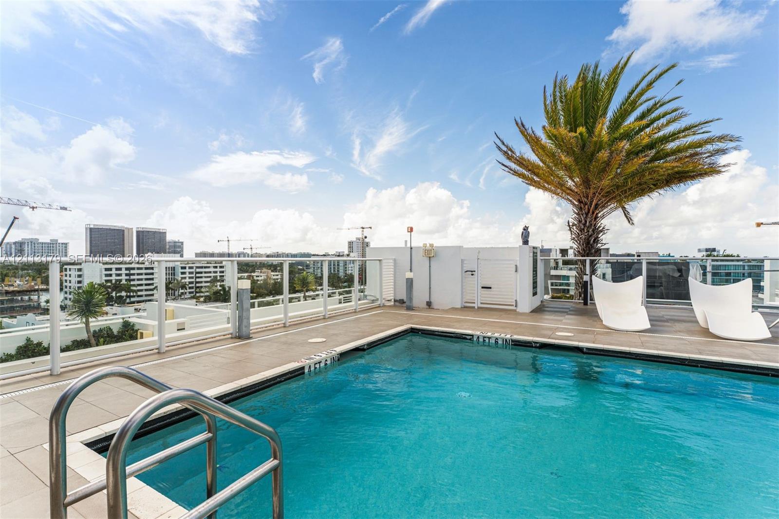 Rooftop swimming pool featuring large-format tile decking, glass perimeter railing, and stainless steel ladder