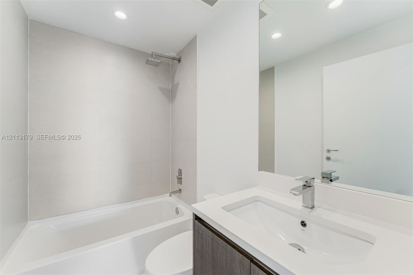Bathroom featuring a large-format tiled shower surround with a rain-style showerhead, a deep soaking tub, and a vanity topped with a rectangular integrated sink and a chrome single-handle faucet