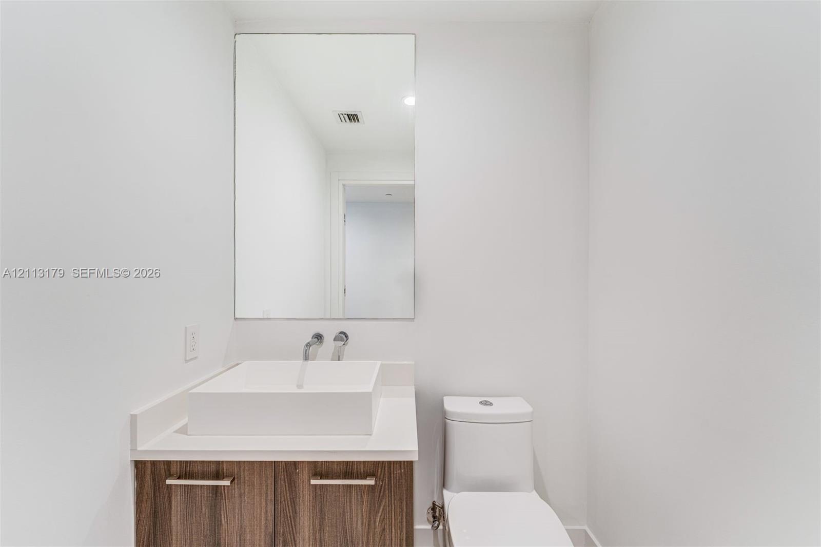 Floating wood-finish vanity with a rectangular vessel sink, solid-surface countertop, wall-mounted faucet, and a large frameless mirror
