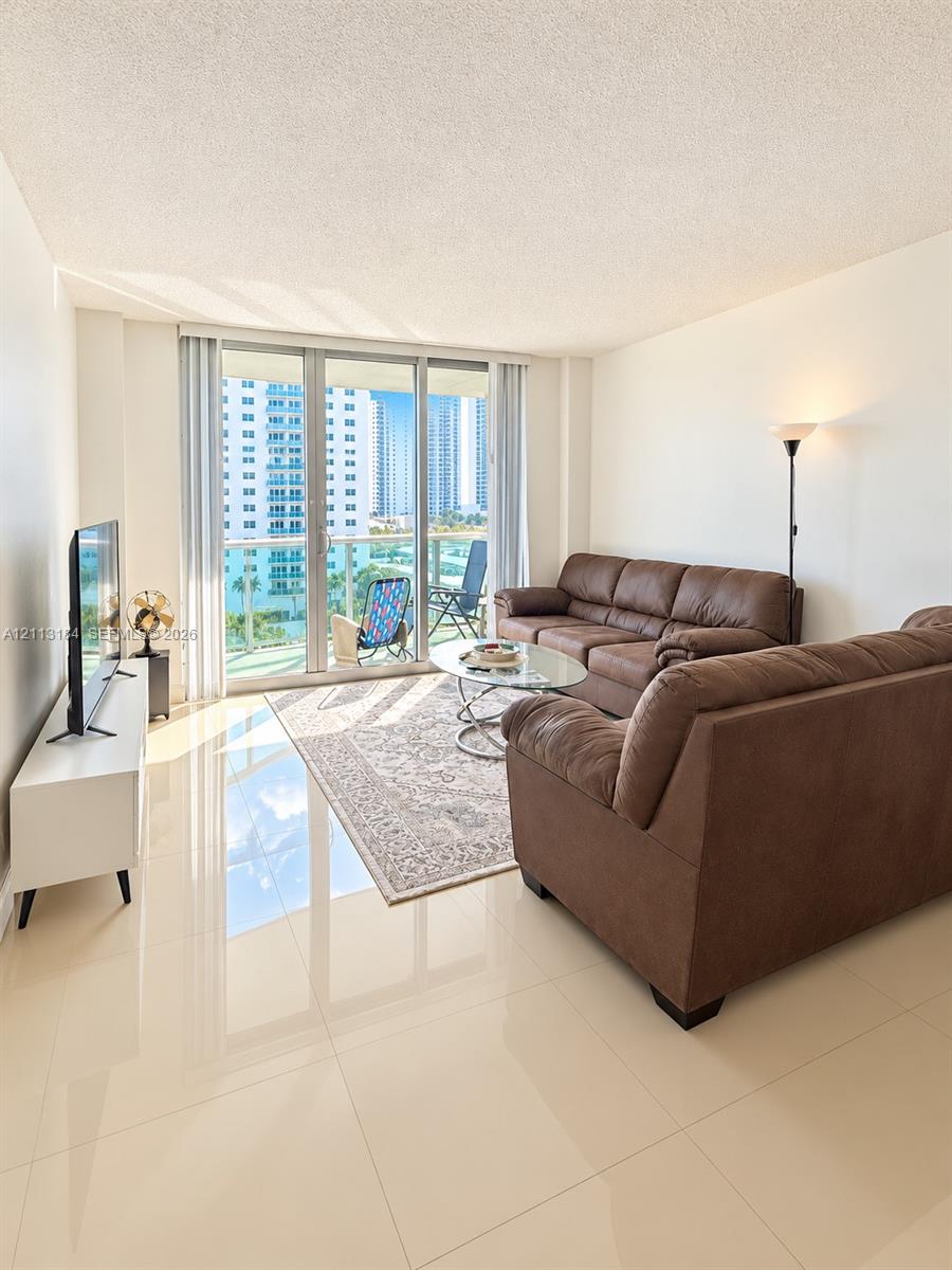Living area featuring polished tile flooring, floor-to-ceiling windows, and access to a private balcony