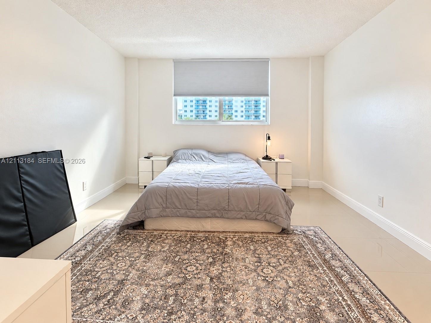 Neutral-toned interior featuring smooth wall finishes, large-format tile flooring, and a window with an integrated roller shade