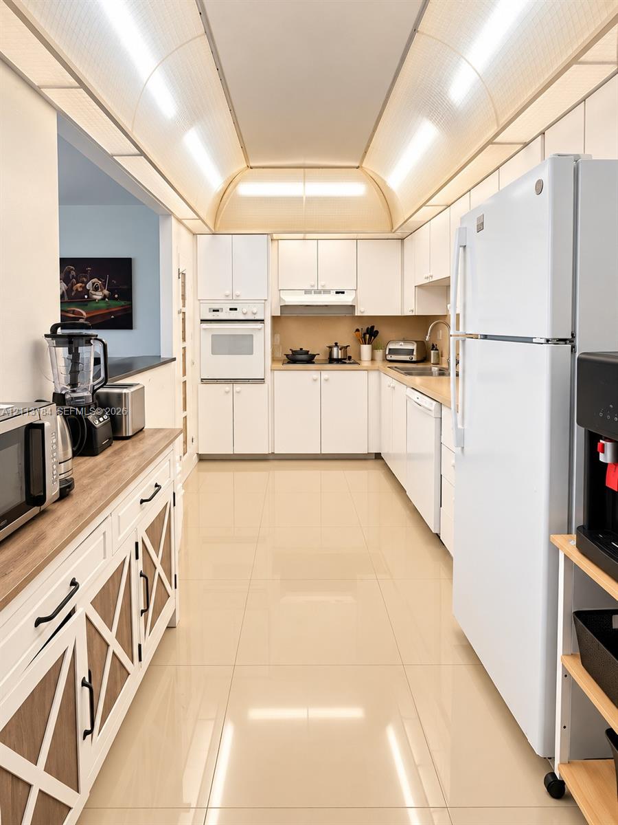 Kitchen featuring a barrel-vaulted ceiling, high-gloss tile flooring, white cabinetry with integrated appliances, and a wood-finish countertop