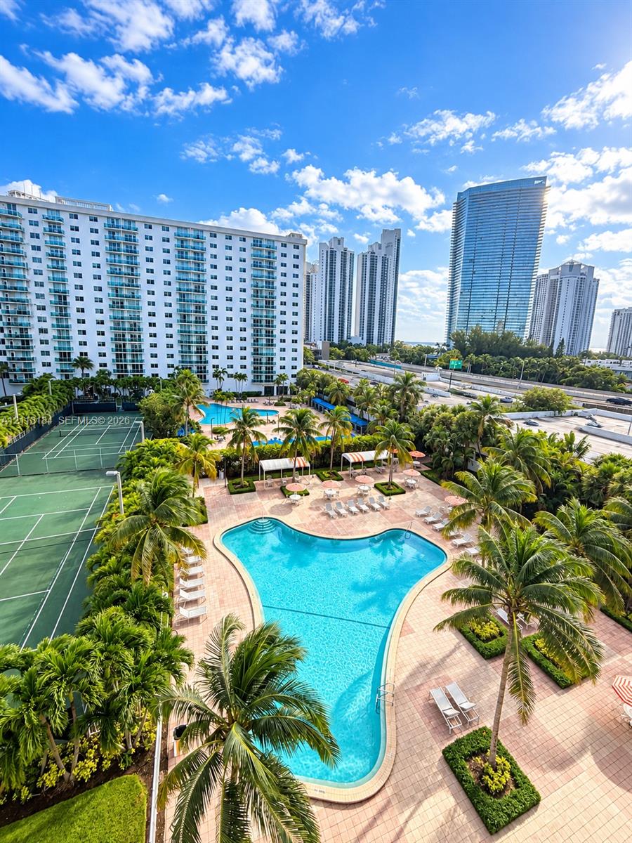 Community amenities including a swimming pool, tennis court, palm-lined hardscaping, and manicured landscaping