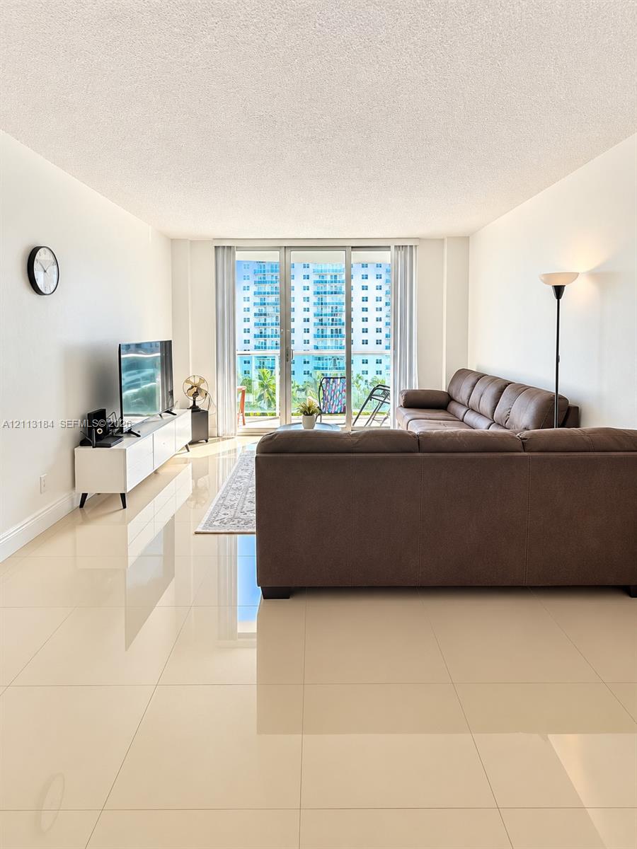 Living area featuring polished large-format tile flooring and floor-to-ceiling glass sliding doors opening to a balcony