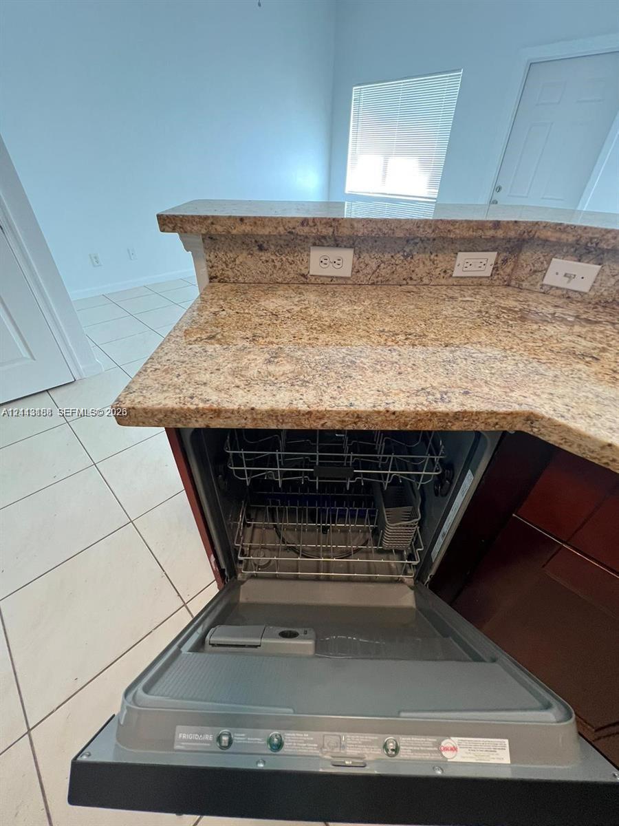 Kitchen area featuring stone-surfaced countertops, a breakfast bar, ceramic tile flooring, and an integrated Frigidaire dishwasher