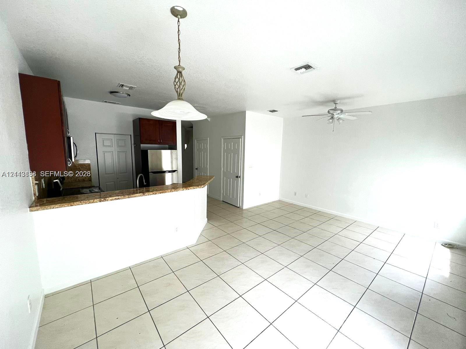 Kitchen featuring stone-finish countertops, dark wood-tone cabinetry, stainless steel appliances, ceramic tile flooring, and a pendant light fixture