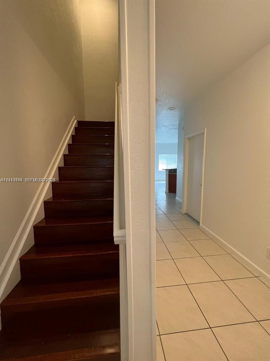 Staircase featuring wood-finish treads and white railing, paired with large-format ceramic tile flooring