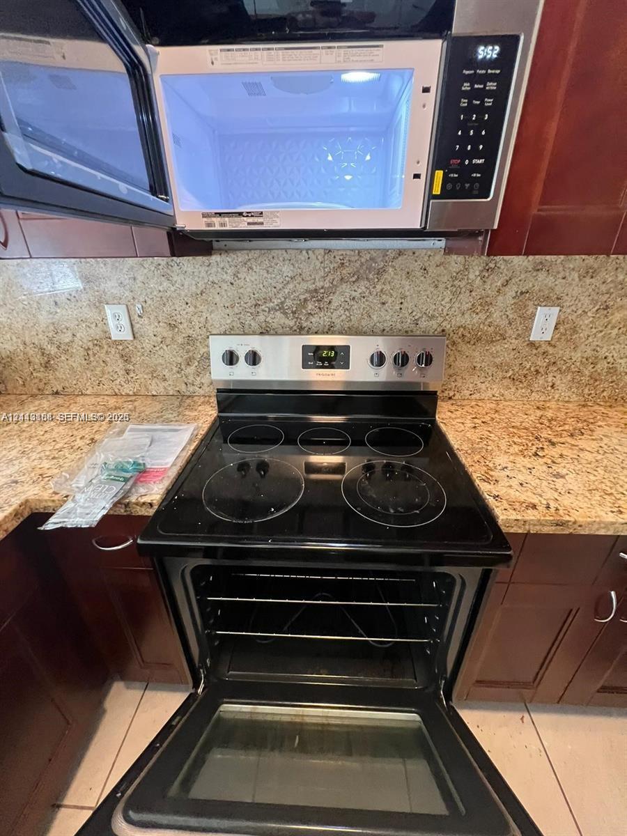 Stainless steel electric range with a glass cooktop and matching over-the-range microwave, set against stone-surface countertops and dark wood-finish cabinetry