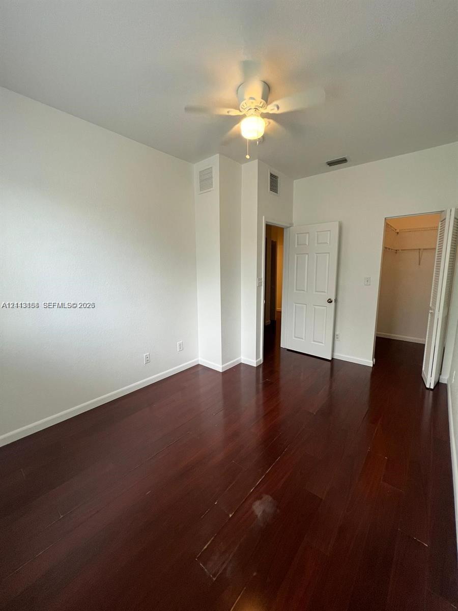 Room featuring wood-finish flooring, a white ceiling fan with integrated lighting, and a walk-in closet with built-in shelving
