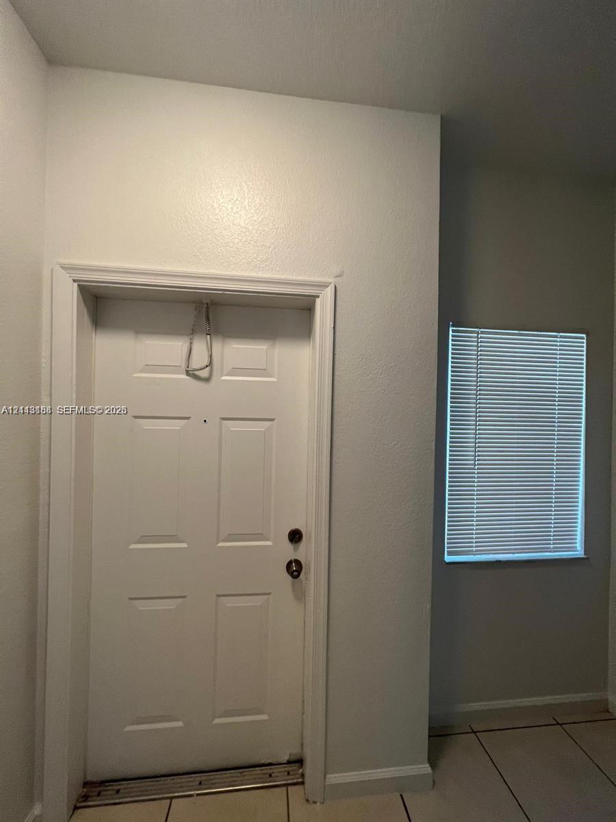 Six-panel door with metallic hardware, recessed peephole, and neutral-toned ceramic tile flooring