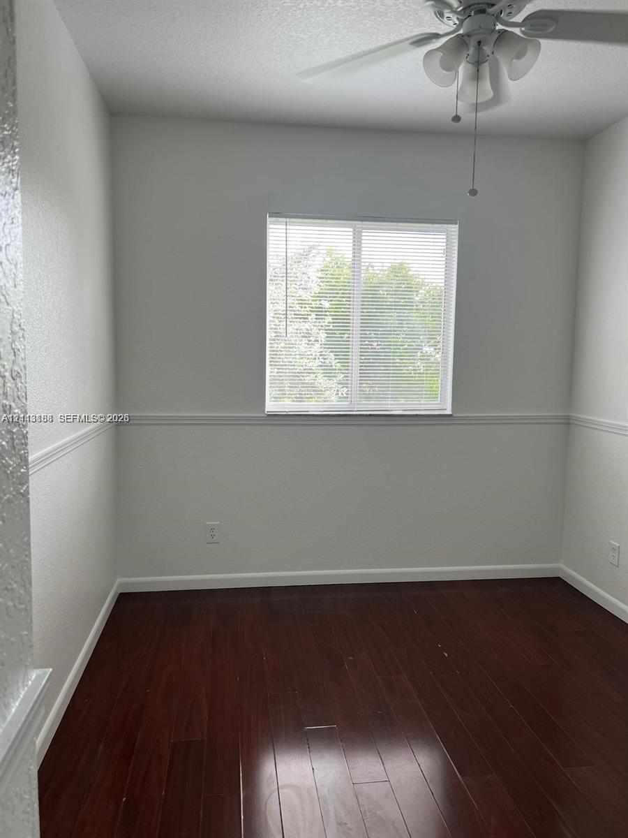 Room interior featuring wood-finish flooring, a ceiling fan with integrated lighting, a single-pane sliding window, and chair rail molding