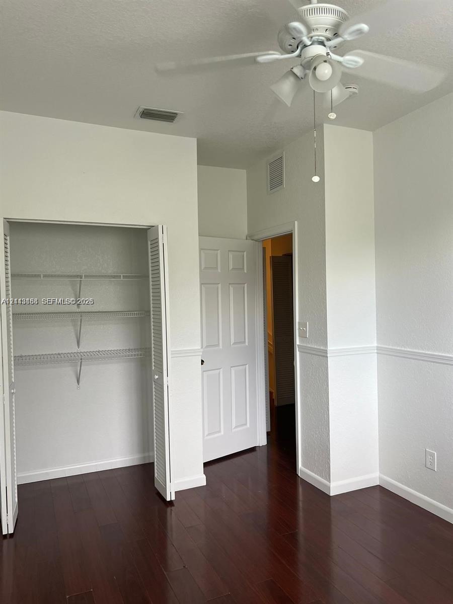 Wood-finish flooring, ceiling fan with integrated lighting, reach-in closet with built-in wire shelving, and traditional chair rail molding