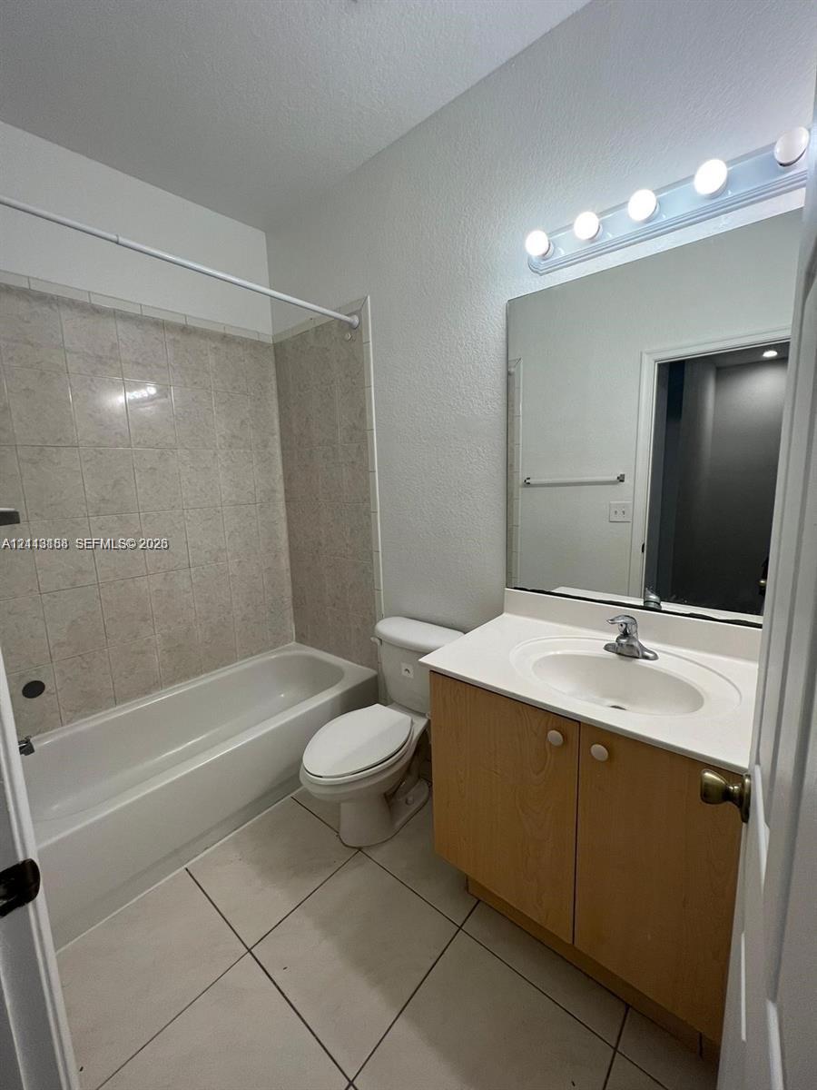 Full bathroom featuring a vanity with integrated sink, large wall-mounted mirror, multi-bulb vanity light, and a tub with tiled surround