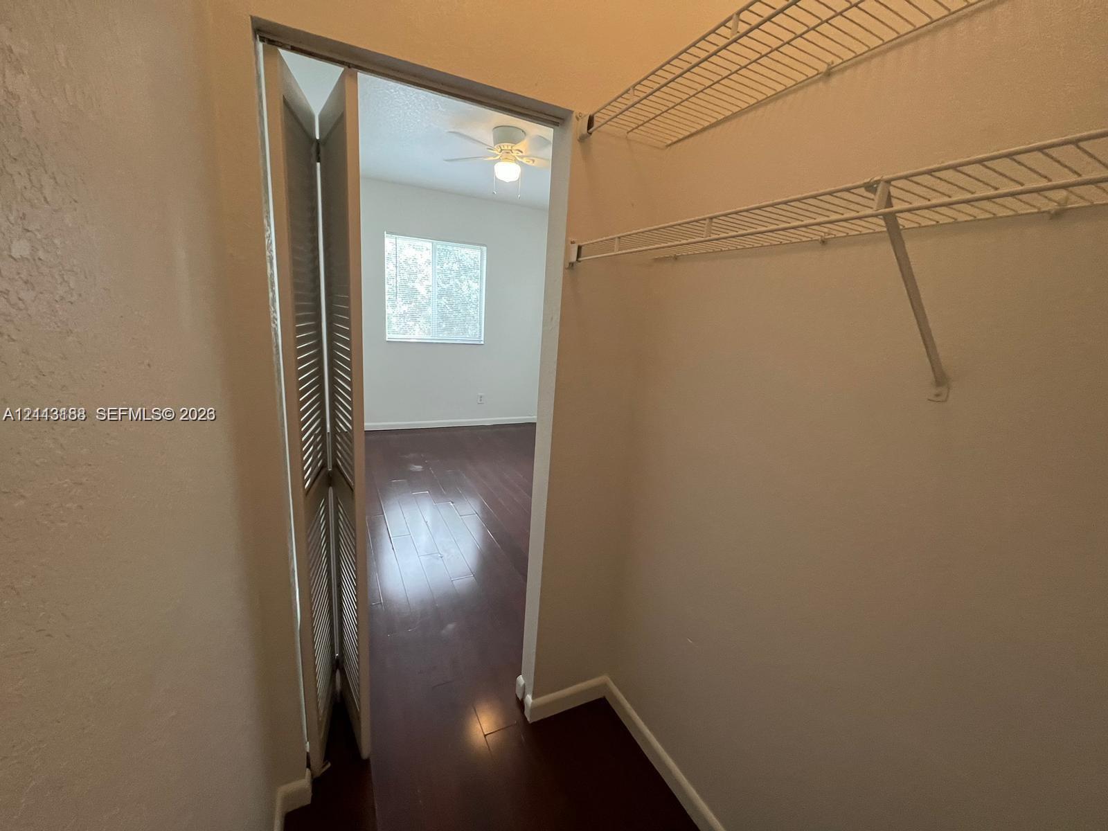 Closet featuring white wire shelving and bi-fold louvered doors, with wood-finish flooring, ceiling fan, and window visible in the background