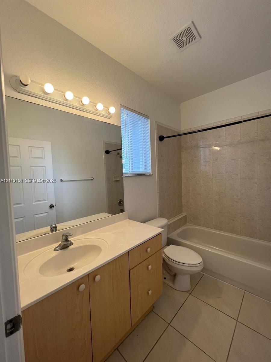 Bathroom featuring a vanity with light-wood cabinetry, white solid-surface countertop, integrated basin, wall-mounted mirror, and tile flooring