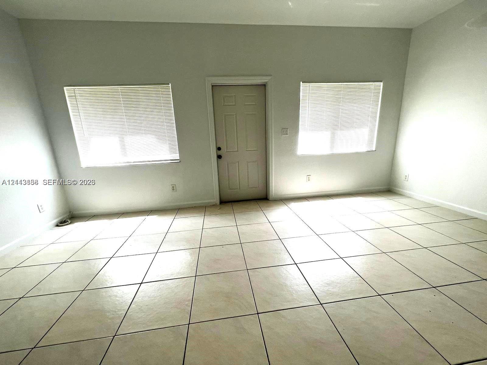 Interior space featuring large-format ceramic tile flooring, neutral wall tones, two dual-pane windows, and a central solid-panel entry door