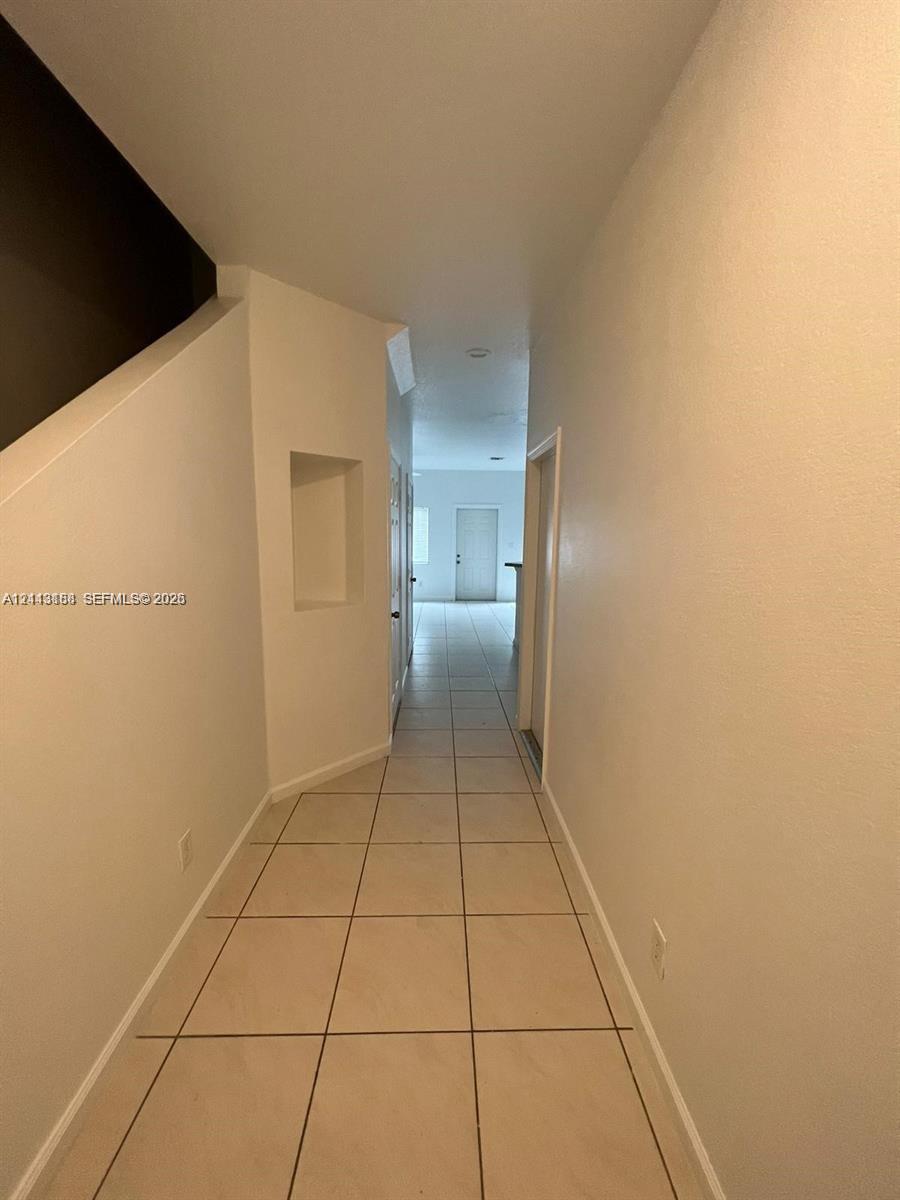 Hallway featuring neutral-tone tile flooring, built-in recessed wall niche, and smooth-finish walls