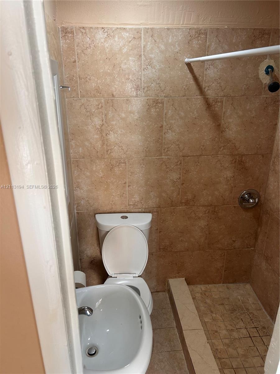 Full-height wall tile, tiled shower surround, integrated shower floor, porcelain toilet, and wall-mounted sink