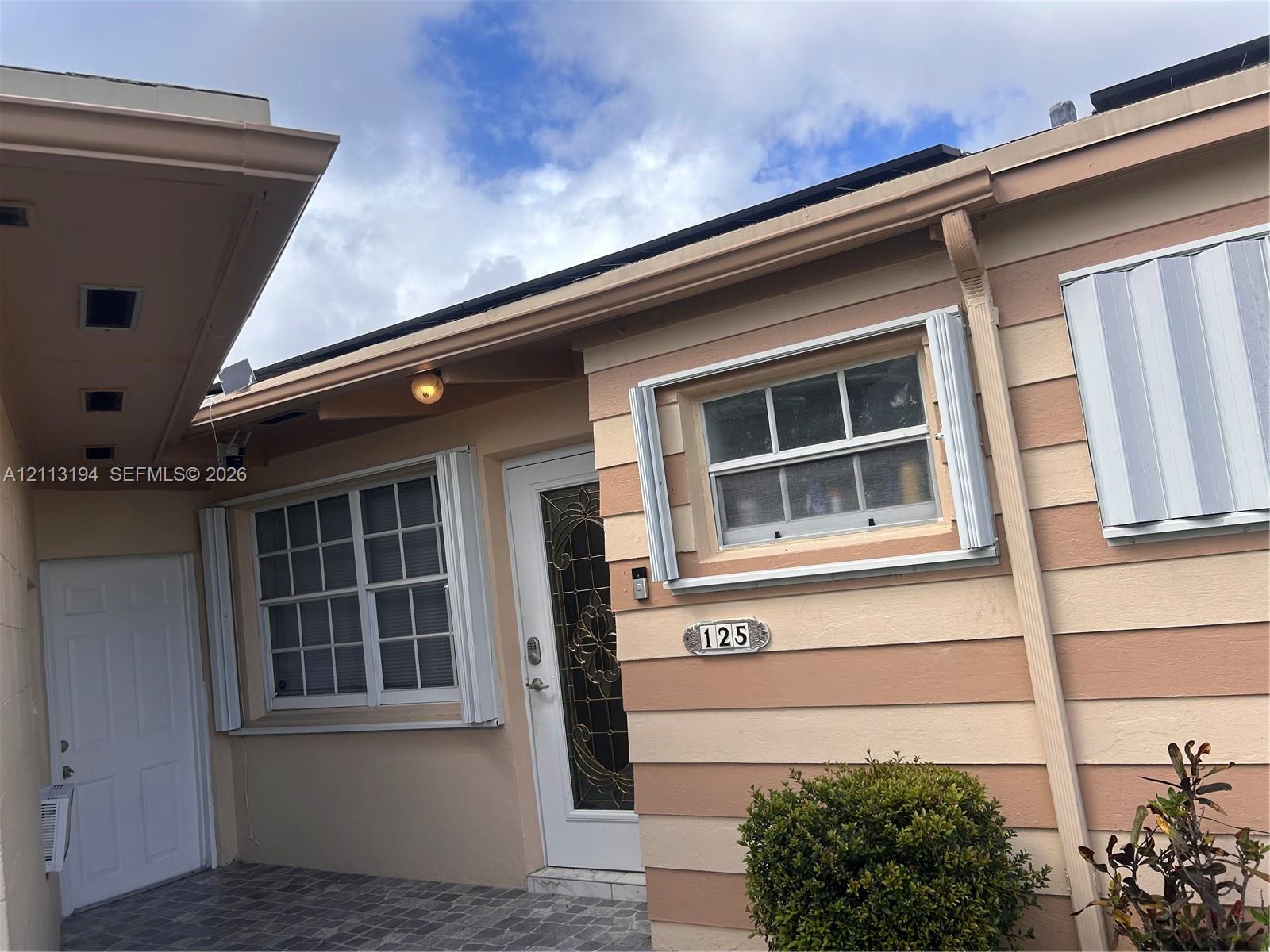 Exterior facade featuring horizontal two-tone siding, grid-patterned windows, decorative glass entry door, and stone-finish paved entry area Exterior facade featuring horizontal two-tone siding, grid-patterned windows, decorative glass entry door, and stone-finish paved entry area