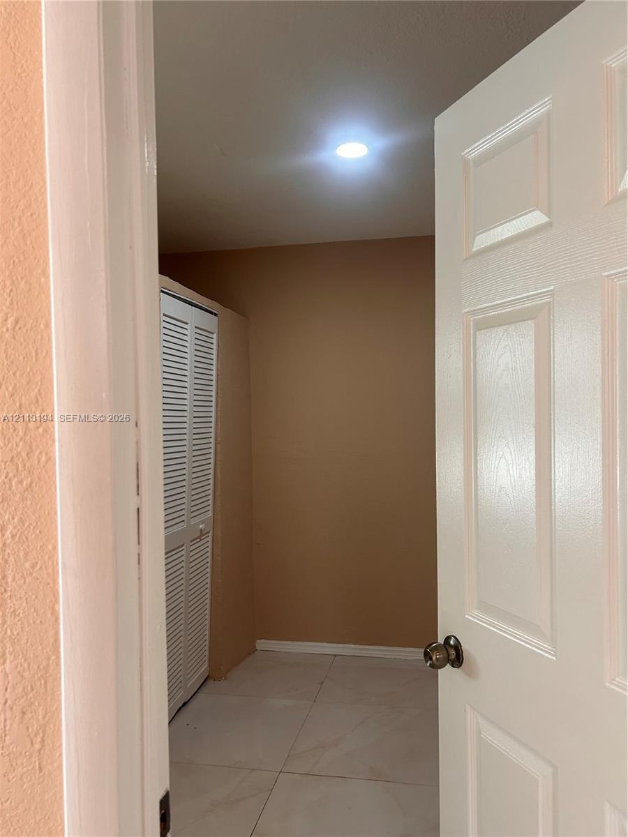 Interior space featuring large-format tile flooring, recessed ceiling lighting, and white louvered-panel closet doors