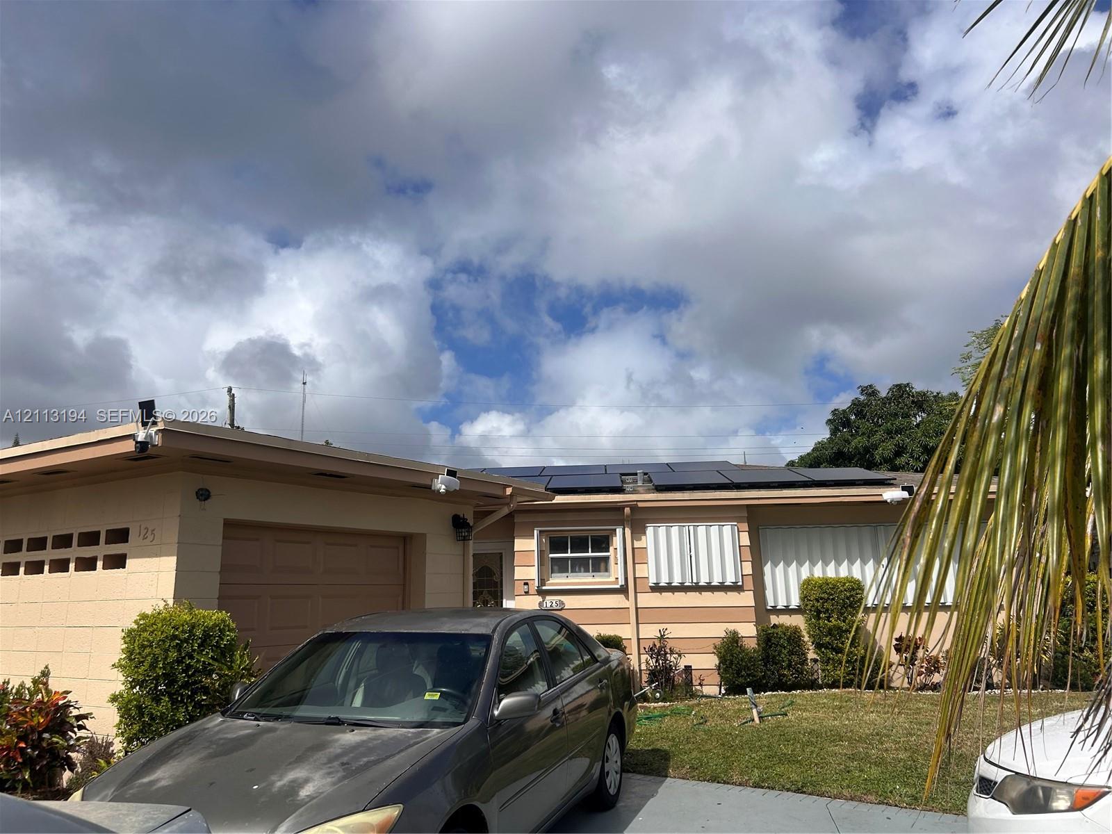 Single-story exterior featuring a concrete block facade, an attached garage, and roof-mounted solar panels Single-story exterior featuring a concrete block facade, an attached garage, and roof-mounted solar panels