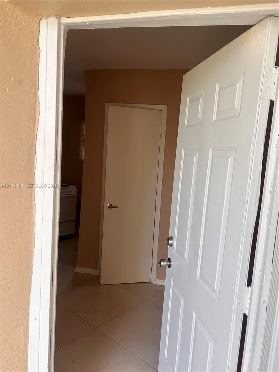 White six-panel interior door with metallic hardware, neutral wall paint, and light-toned tile flooring