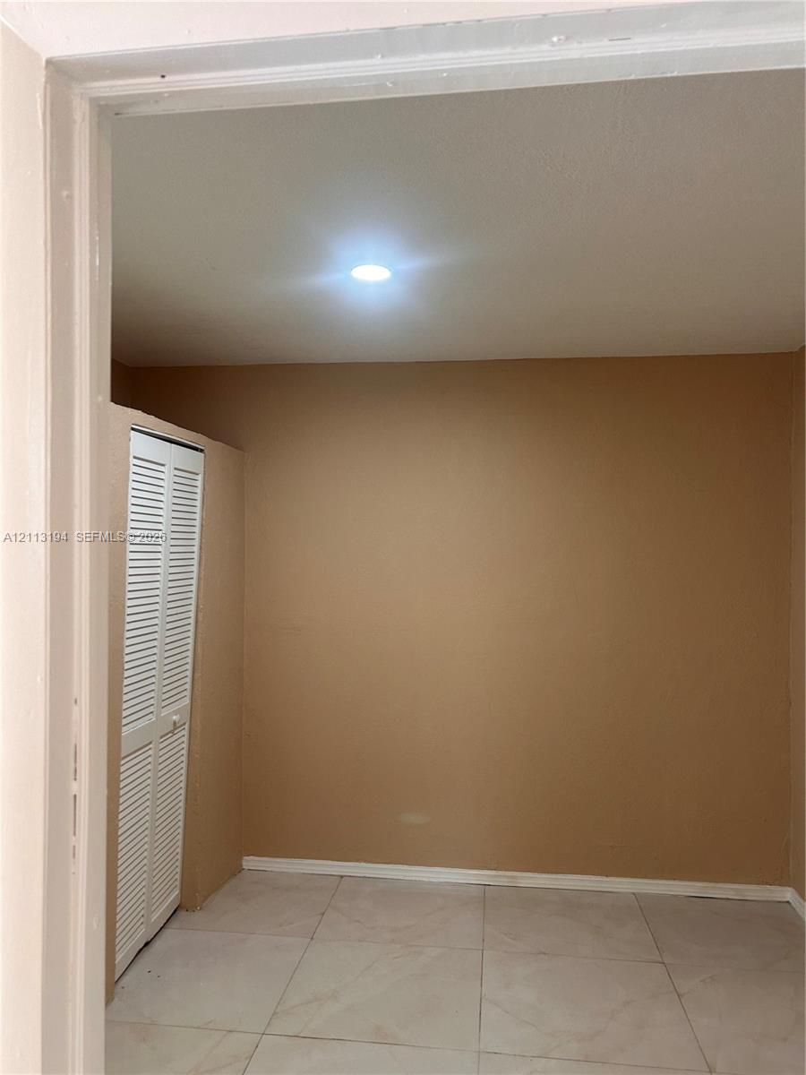 Neutral-toned interior room featuring large-format tile flooring, recessed lighting, and a built-in closet with white louvered doors