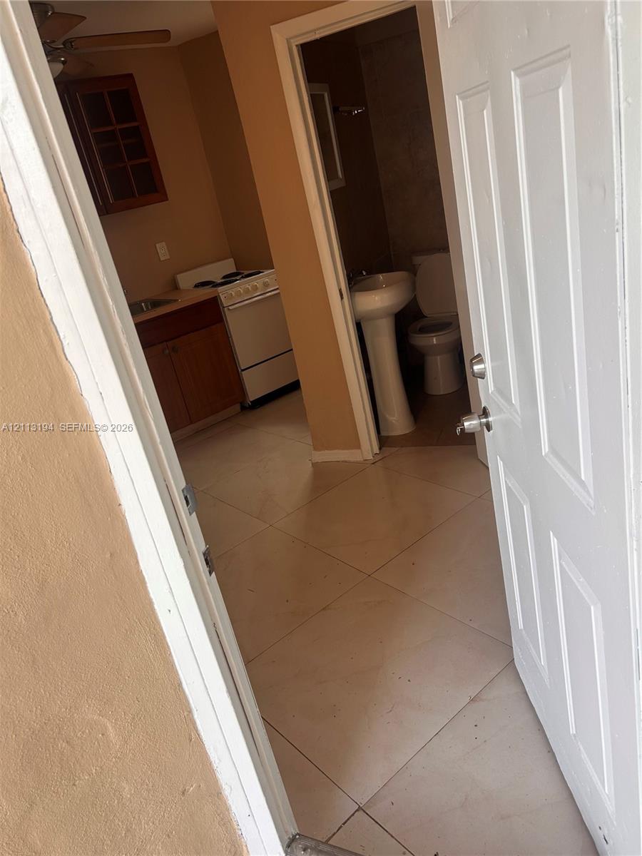 Interior space featuring large-format ceramic floor tiling, wood-finish cabinetry, a white freestanding range, and a pedestal sink Interior space featuring large-format ceramic floor tiling, wood-finish cabinetry, a white freestanding range, and a pedestal sink