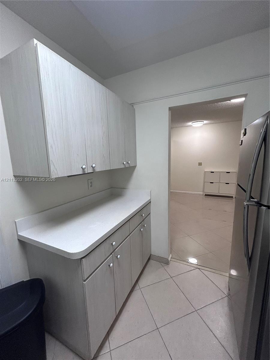 Light-toned wood-finish cabinetry, solid-surface countertops, and diagonal-pattern tile flooring