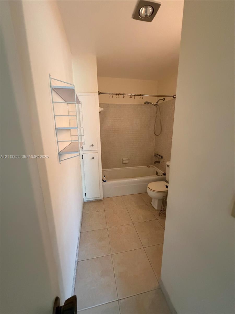 Bathroom featuring tile flooring, a shower and tub combination with tiled surround, and built-in vertical cabinetry