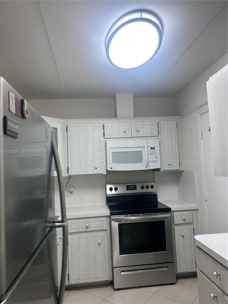 Kitchen featuring light-finish cabinetry, stainless steel refrigerator and range, over-the-range microwave, and overhead flush-mount lighting