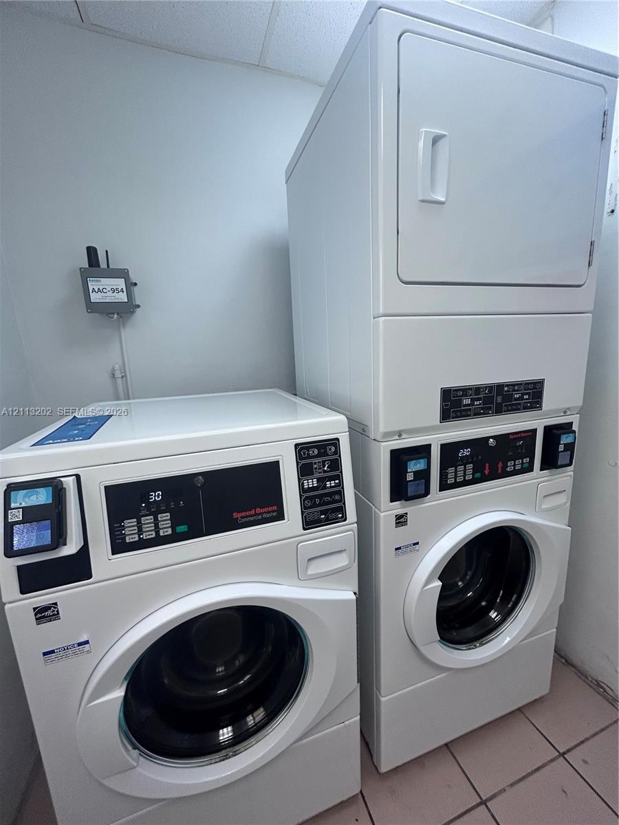 Commercial-grade front-loading washer and stackable dryer unit with digital control interfaces and tile flooring