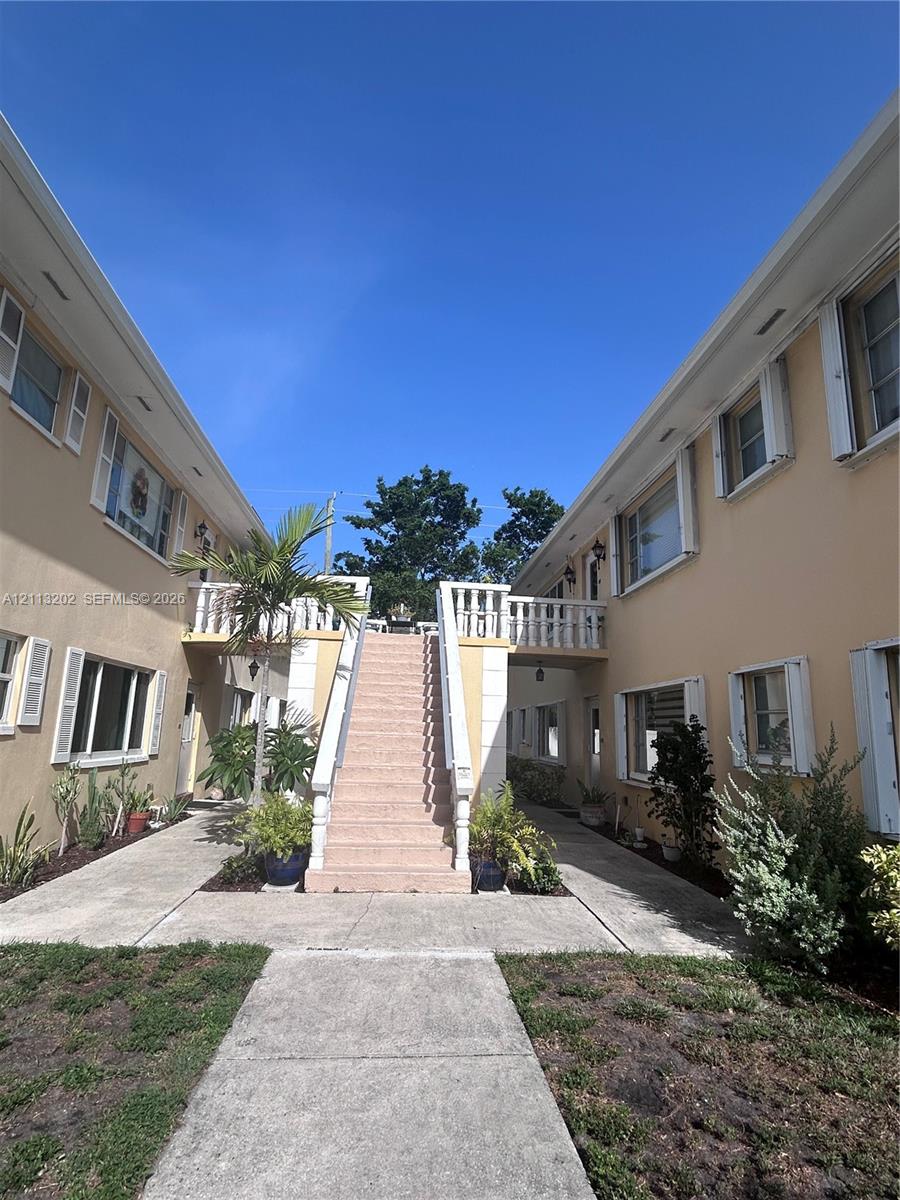 Stucco exterior featuring a central stone staircase, balustrade railings, shuttered windows, and concrete walkways